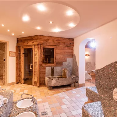 Ein entspannender Wellnessbereich mit einer Sauna aus Holz und steinernen Liegen. Sanfte Beleuchtung und eine ruhige Atmosphäre laden zur Erholung ein.