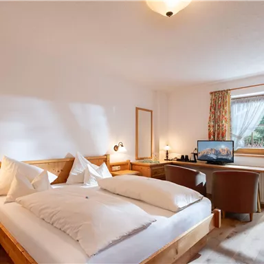 Ein gemütliches Schlafzimmer mit einem Doppelbett und einem Schreibtisch. Das Zimmer hat helle Wände, natürliche Holzdetails und einen Blick nach draußen durch große Fenster.