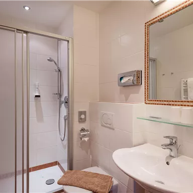 Ein modernes Badezimmer mit Dusche und Waschbecken. Saubere, helle Fliesen und Handtücher ergänzen den Raum.