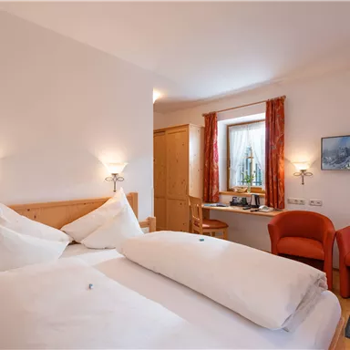 Ein gemütliches Zimmer mit einem Doppelbett und hellen, einladenden Farben. Am Fenster stehen zwei rote Sessel und ein Tisch mit einem schönen Ausblick.
