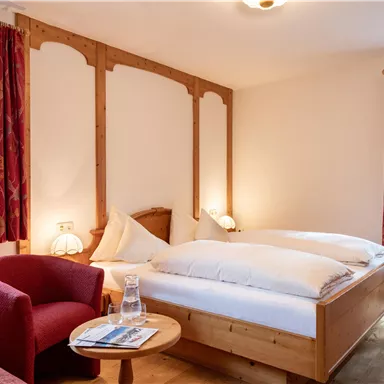 Ein gemütliches Schlafzimmer mit einem Doppelbett und roten Vorhängen. Ein runder Tisch mit einem Wasserglas und einem Stuhl bietet einen einladenden Platz zum Entspannen.