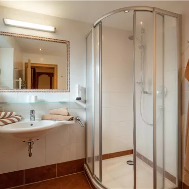 Ein modernes Badezimmer mit einer Duschkabine und einem Waschbecken. Die Wände sind in hellen Farben gehalten, und es gibt natürliche Lichtquellen durch Fenster.