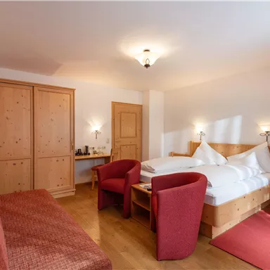 Ein gemütliches Schlafzimmer mit einem Doppelbett, einem Fernseher und zwei roten Stühlen. Der Raum ist hell und freundlich eingerichtet, mit Holzregalen und einem roten Teppich.