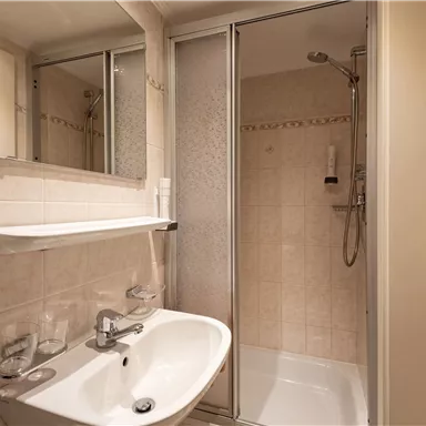 Ein modernes Badezimmer mit Dusche, Spiegel und Waschbecken. Die Wände sind hell gefliest, und es gibt einen Handtuchhalter.