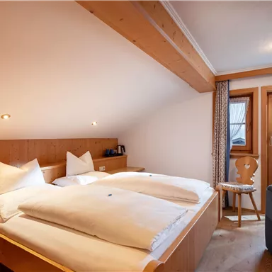 Ein gemütliches Schlafzimmer mit zwei getrennten Betten und Holzelementen. Das Licht ist warm und es gibt einen kleinen Balkon mit Fenster.