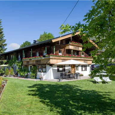 Ein charmantes Holzhaus mit begrünten Außenbereichen und einem schönen Garten. Die Terrasse ist mit Sitzgelegenheiten ausgestattet und es gibt viele Pflanzen im Vordergrund.