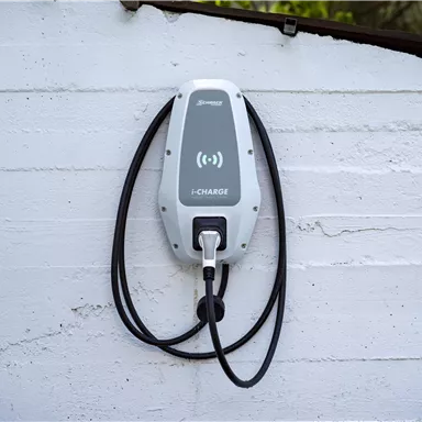 Eine moderne Elektroauto-Ladestation ist an einer Wand montiert. Die Ladestation hat zwei Kabel und ein einfaches, elegantes Design.