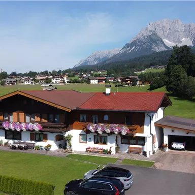 A beautiful house in the countryside, surrounded by green meadows and mountains in the background. The facade of the house is adorned with flowers.
