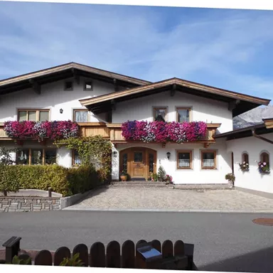 Ein schönes Landhaus mit bunten Blumenkästen an den Fenstern. Der gepflegte Garten und die steinerne Einfahrt verleihen dem Haus einen einladenden Charakter.