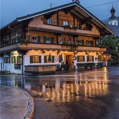 A charming old wooden house on a rainy street. The lights reflect on the wet asphalt.