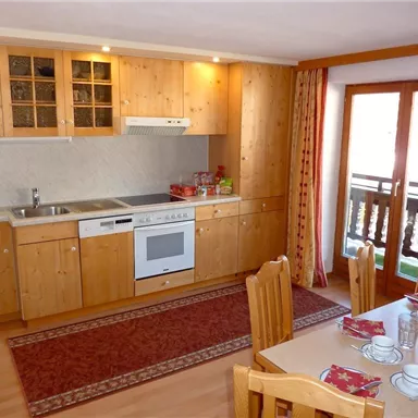 Eine gemütliche Küche mit Holzschränken und modernen Geräten. Der Essbereich ist hell und einladend, mit einem Tisch und Stühlen.