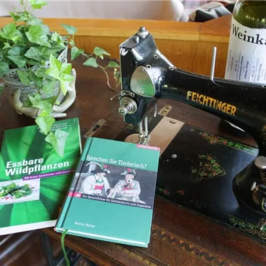 An old sewing machine stands on a table, next to it lie two books. One deals with edible wild plants, the other asks: "Do you speak Tüpfelstück?".