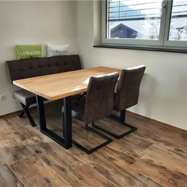 A modern dining room with a wooden tray and comfortable chairs. Large windows provide plenty of daylight and a view outside.