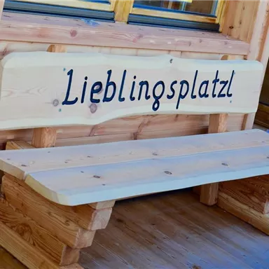 A wooden bench with the inscription "Favorite spot" stands in front of a wooden house. The place looks inviting and cozy.