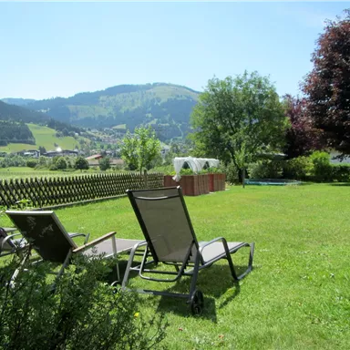Ein schöner Garten mit Liegestühlen und Blick auf die Berge. Die Landschaft ist grün und sonnig.