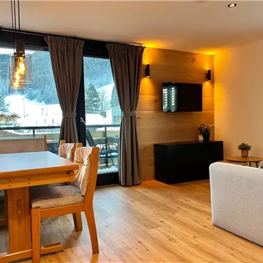 A modern living room with a dining area and a seating landscape. Large windows offer a beautiful view of the mountains.