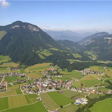 A picturesque landscape with gentle hills and green farmland. In the background, majestic mountains can be seen.
