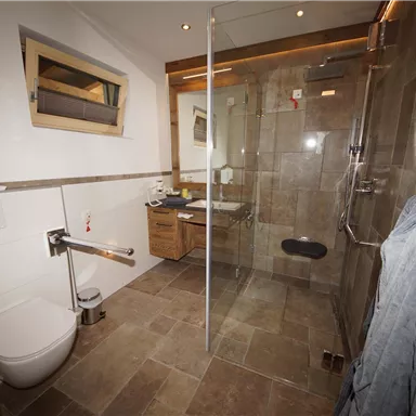 A modern bathroom with a walk-in shower and a toilet. Light-tiled walls and warm wood accents create an inviting atmosphere.