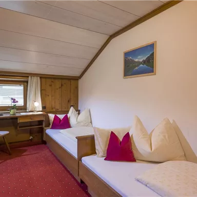 A cozy room with two beds, a small table, and a window. A picture of a mountain landscape hangs on the wall.