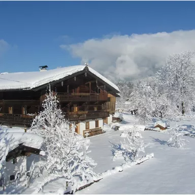A cozy chalet in the snow with an impressive landscape. The trees are covered with a thick layer of snow and the sky is partly cloudy.