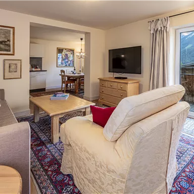 A cozy living area with a bright sofa, a table, and a television. Large windows offer a beautiful view outside.