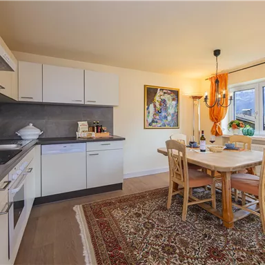A bright and modern kitchen with a dining area. The table is made of wood and the walls are decorated with orange embellishments.