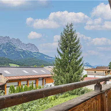 A picturesque view of the mountains with a church in the foreground. The sky is clear and the surroundings are green and inviting.
