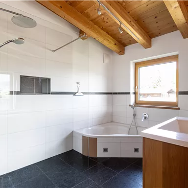 A modern bathroom with a shower and a bathtub. The wooden beam ceiling gives the room a warm atmosphere.