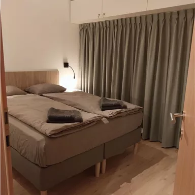 A cozy bedroom with a double bed and soft, neutral colors. Curtains and a wooden floor give the room a warm atmosphere.