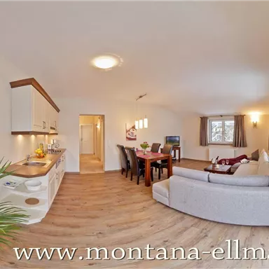 A modern living room with hardwood floors and a comfortable couch. The room has large windows with a view outside and an inviting dining area.