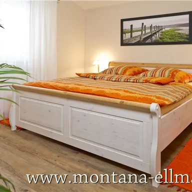 A cozy bedroom with a large bed and orange pillows. In the background, there is a window and a picture on the wall.