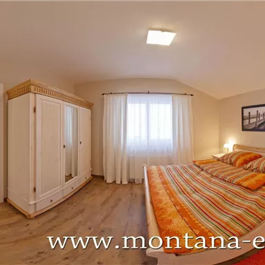 A cozy bedroom with a large double bed and colorful bedspreads. The room has bright walls and a window view that lets in natural light.