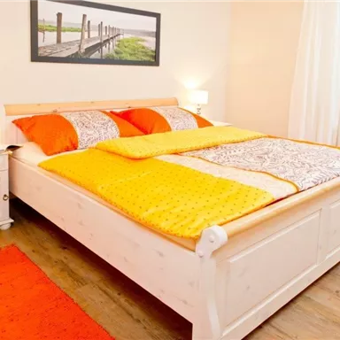 A cozy bedroom with a large bed and colorful quilts. Comfortable lighting and wooden flooring create an inviting atmosphere.
