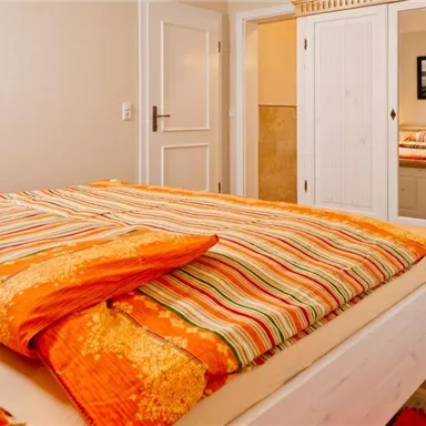 A cozy bedroom with a large bed and colorful bedspreads. In the background, a mirror and a door can be seen.