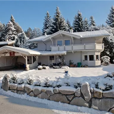 Unser Haus im Schnee, umgeben von schneebedeckten Bäumen.