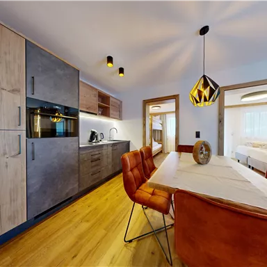 Eine moderne Küche mit Holzschränken und einem elegante Tisch mit ledigen Stühlen. Die Atmosphäre ist hell und einladend, ideal für geselliges Beisammensein.