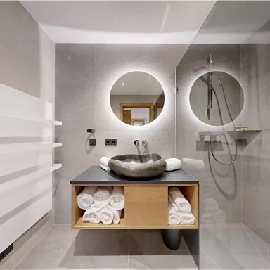 Ein modernes Badezimmer mit einer eleganten Waschschüssel und runden Spiegeln. Handtücher sind ordentlich auf einem Regal angeordnet.