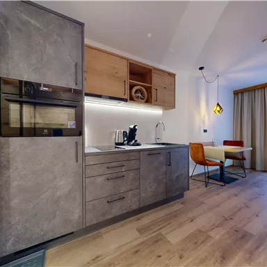 Eine moderne Küchenzeile mit grauen Schränken und Holzdetails. Der Raum ist hell und minimalistisch eingerichtet, mit einem kleinen Esstisch und einem Stuhl.