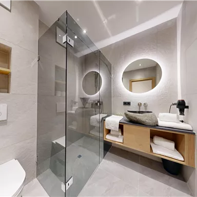 Ein modernes Badezimmer mit einer Glasdusche und stilvollen Holzregalen. Der Raum ist hell und minimalistisch gestaltet.