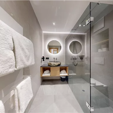 Ein modernes Badezimmer mit gläserner Dusche und minimalistischer Ausstattung. Es bietet helle Wände, einen großen Wandspiegel und frische Handtücher.