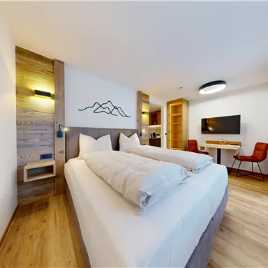 Ein modernes Hotelzimmer mit einem großen Bett und Holzverkleidung. Im Hintergrund sind ein Fernseher und ein Schreibtisch zu sehen.