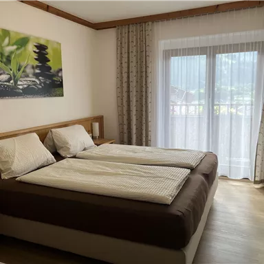 A bright room with two single beds and windows that let in plenty of daylight. A calm picture of plants and stones hangs on the wall.