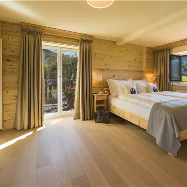 A modern bedroom with wooden paneling and large windows. The room is bright and inviting with a large bed and cozy furnishings.
