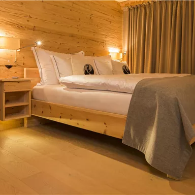 A modern bedroom with a large bed and wooden panels. The soft lighting and curtains create a cozy atmosphere.