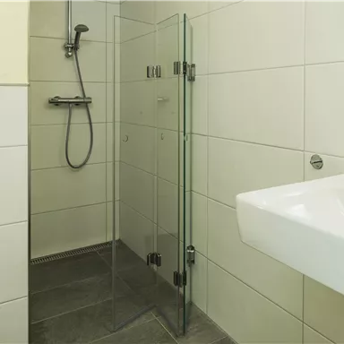 A modern bathroom with a glass shower and a sink. The walls are tiled with light tiles.