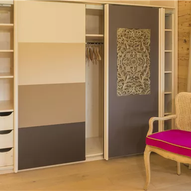 A modern wardrobe with sliding doors in soft colors stands next to an elegant chair with a pink cushion. The room feels bright and inviting.