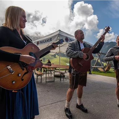 A group of musicians is playing outside. They are wearing traditional clothing and the atmosphere is festive.