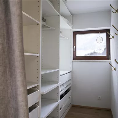 A modern room with white shelves and a window. Some hooks for clothes are attached to the wall.
