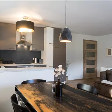 A modern kitchen with a large dining table and a cozy sofa. The room is bright and cheerfully designed.