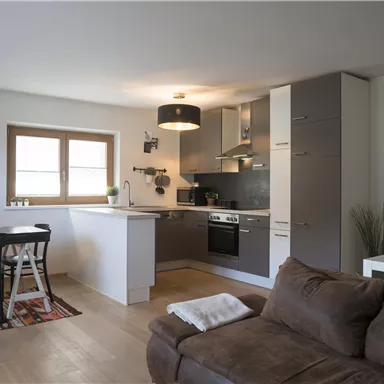 A modern apartment with an open kitchen and a dining area. The space is bright and friendly furnished with a cozy couch.